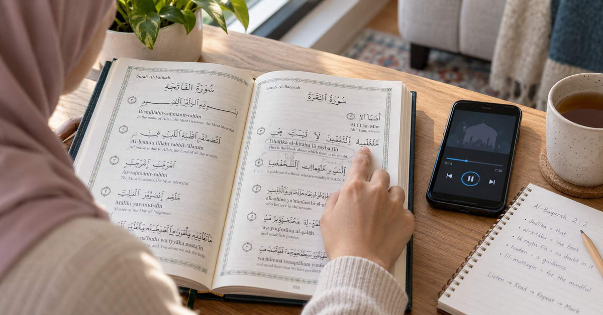 Beginner following Quran transliteration with a finger while listening to audio recitation on a smartphone, with study notes beside the open Quran.