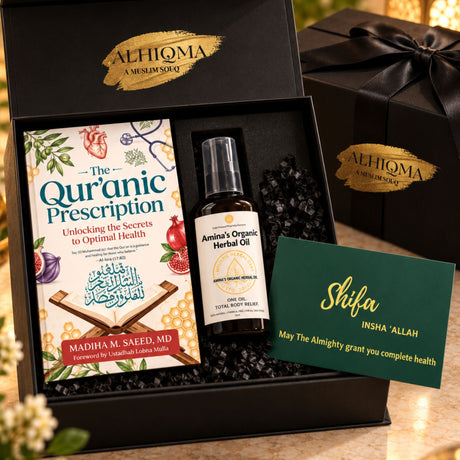 A curated wellness gift set in a black presentation box, featuring 'The Quranic Prescription' book, 'Amina's Organic Herbal Oil' bottle, a green 'Shifa' card, and a black gift box 